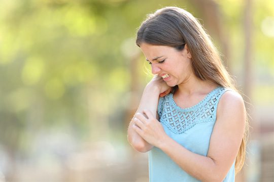 Woman scratching itchy arm outdoors – relieving itchy skin.
