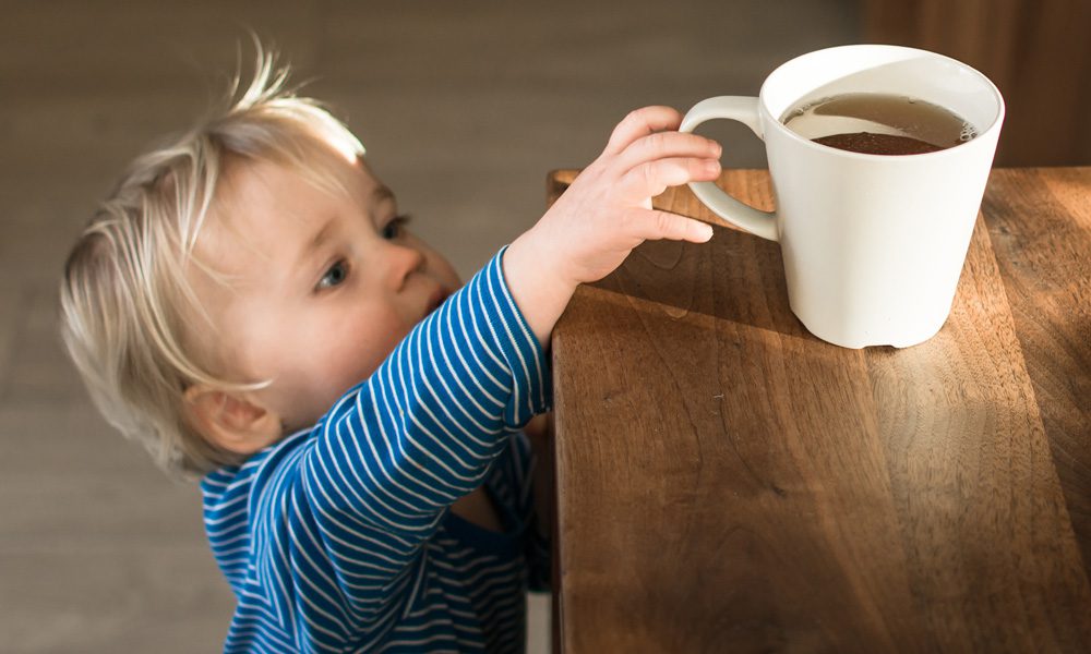 Toddler reaching for a hot drink on a table, showing the risk of hot water scalds in the kitchen